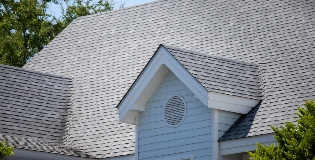 roof shingles on top of the house among a lot of trees. dark asphalt tiles on the roof background