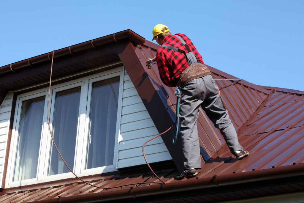 roofer builder worker spraying paint on metal sheet roof