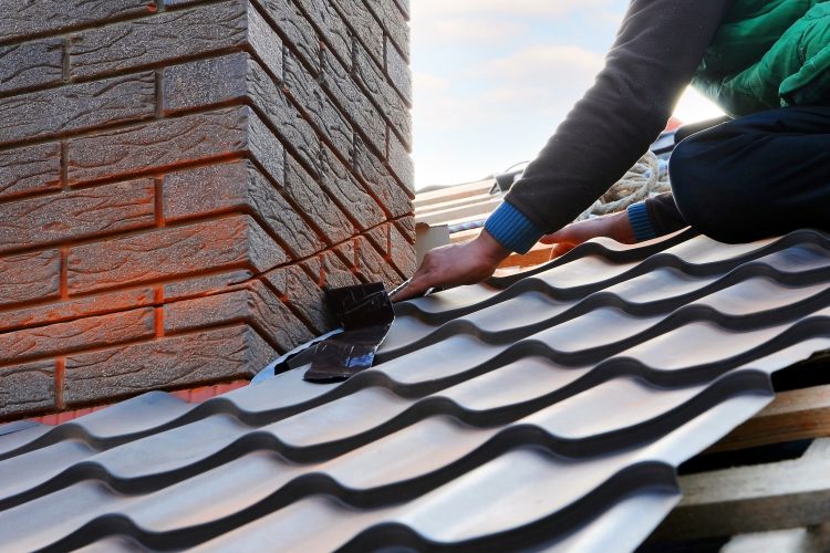 Roofer builder worker attach metal sheet to the chimney. Unfinished roof construction.