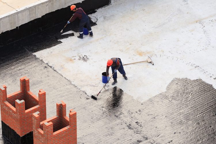 Two workers conduct waterproofing of the roof with bitumen. View from above.