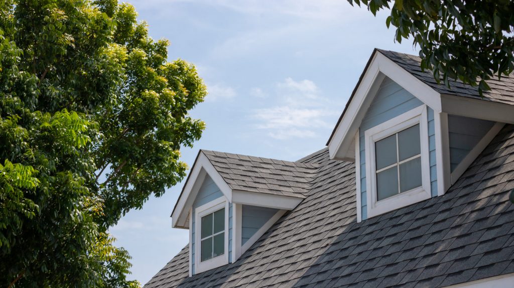 Roof shingles with garret house on top of the house among a lot of trees. dark asphalt tiles on the roof background